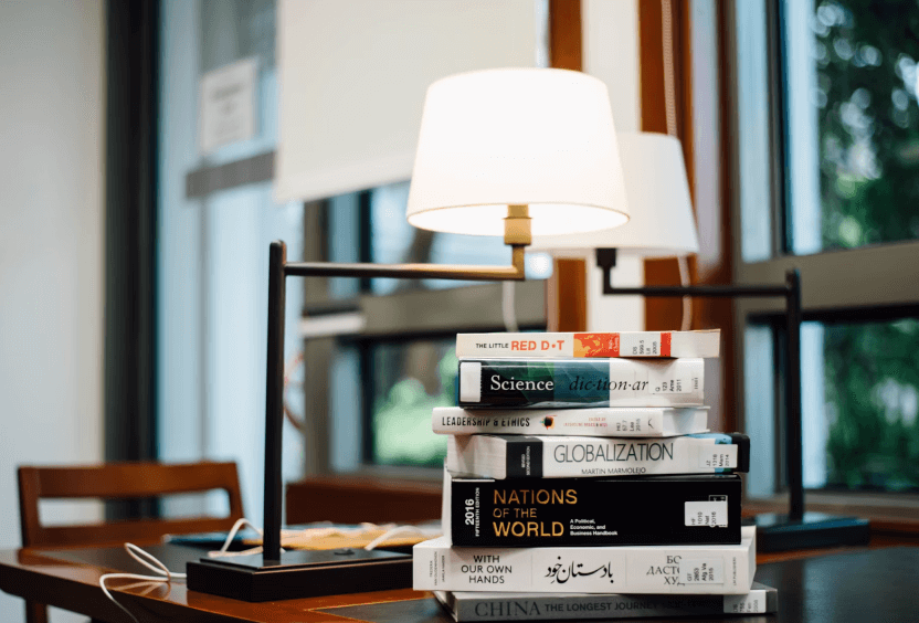 A workspace with a desk, lamp and reference books.